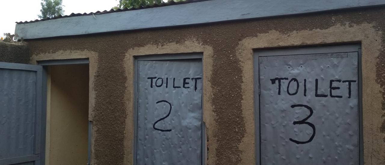 Three toilets, the first door to the toilet is open, the second and third are closed and have Toilet 2 and Toilet 3 written on the doors.