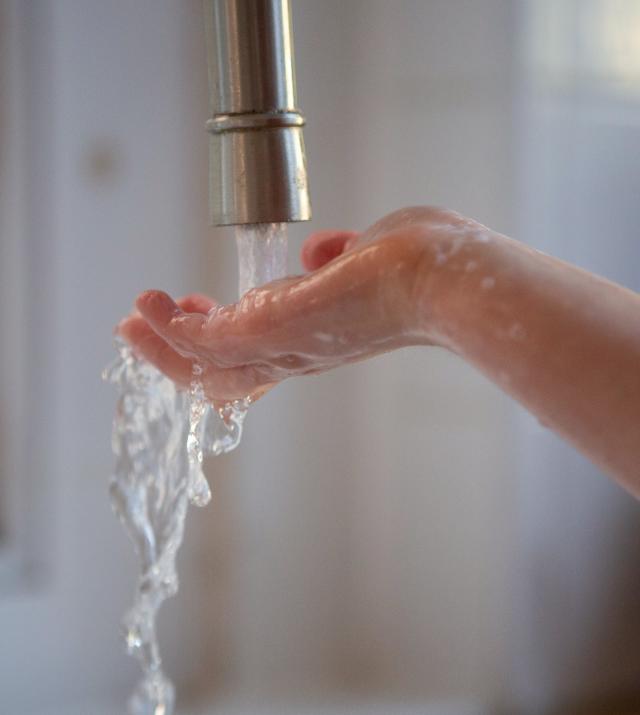 A child holds their hand under a faucet of water.