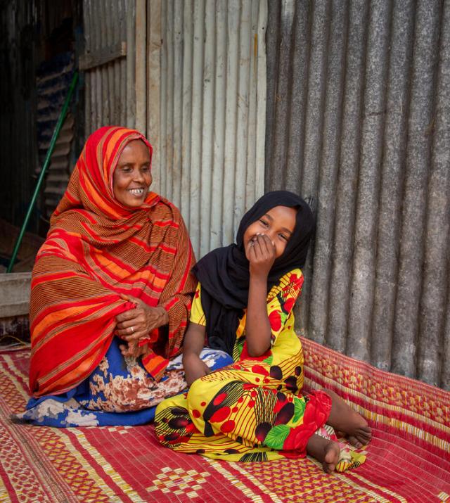 Woman sits with young girl on a floor mat smiling