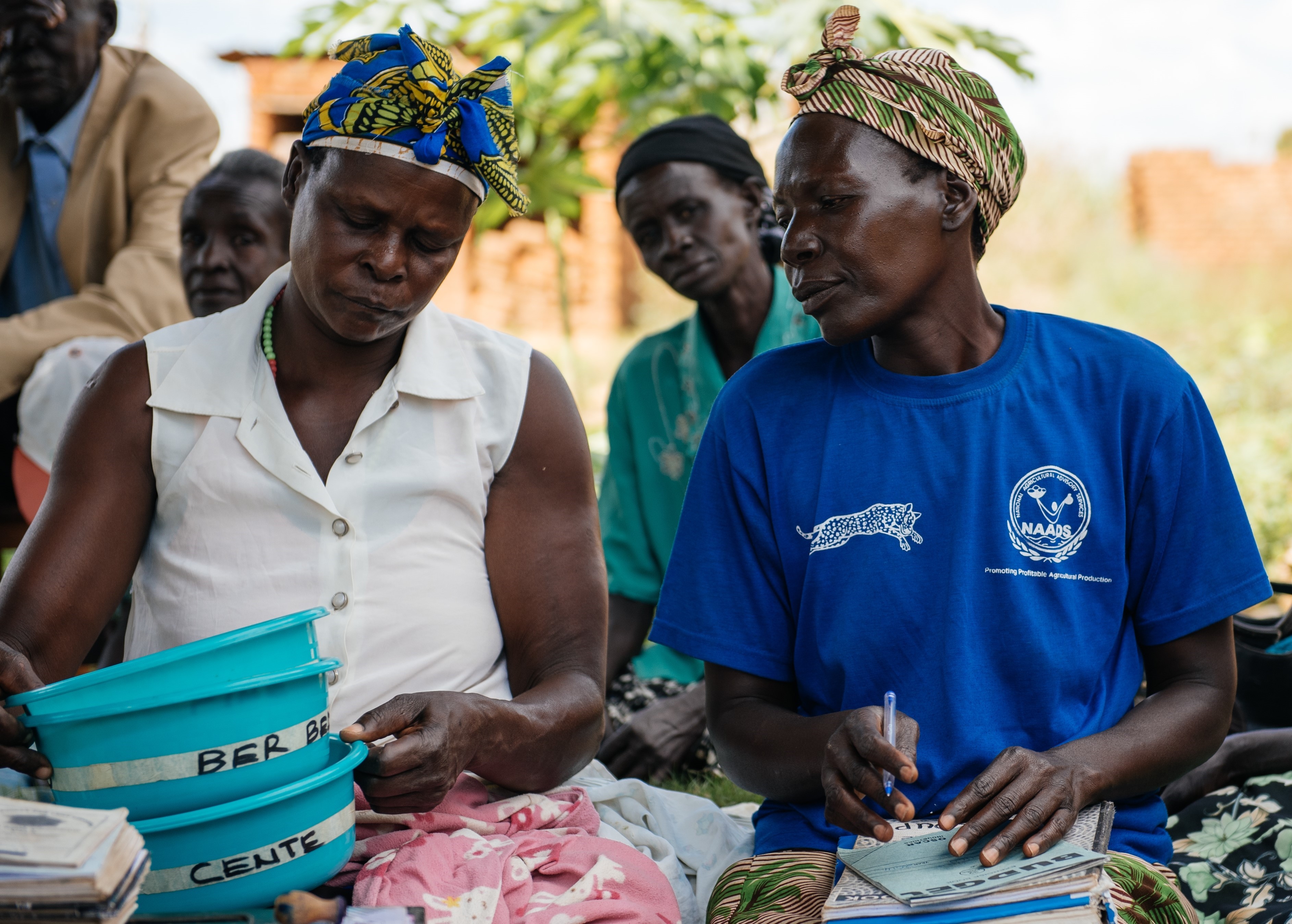 Women organizing savings buckets and notebooks, preparing for a village savings and loans group meeting in Uganda.