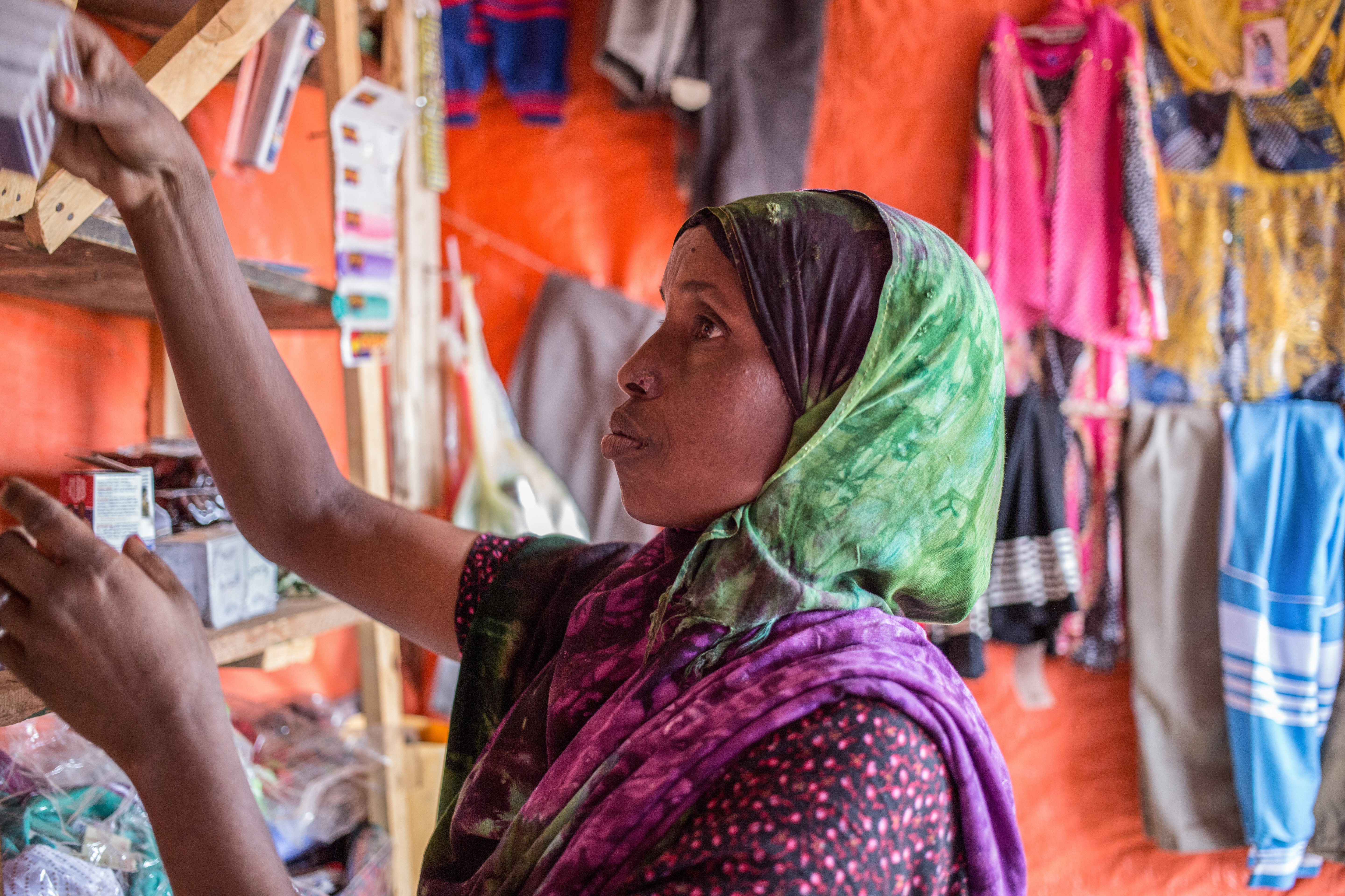 Woman organizing goods on the shelves in her shop in an internally displaced people settlement in Somaliland.