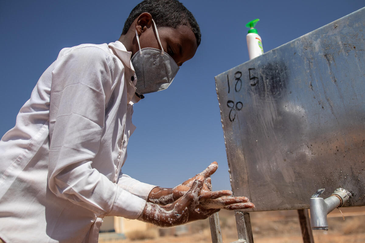 A young boy wearing a mask washes his hands at a handwashing station