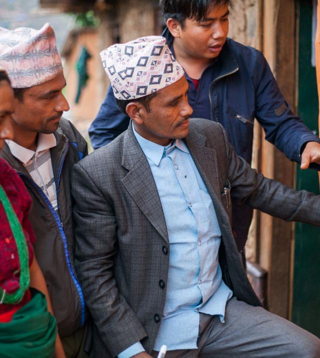 Photo of three Nepalese men and one woman looking and pointing to a posterboard