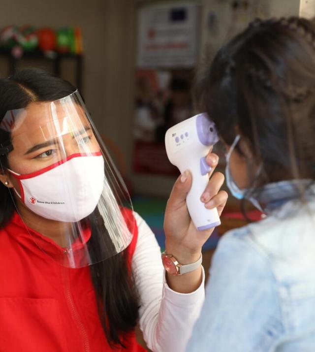 A woman with a mask and face shield takes a child's temperature