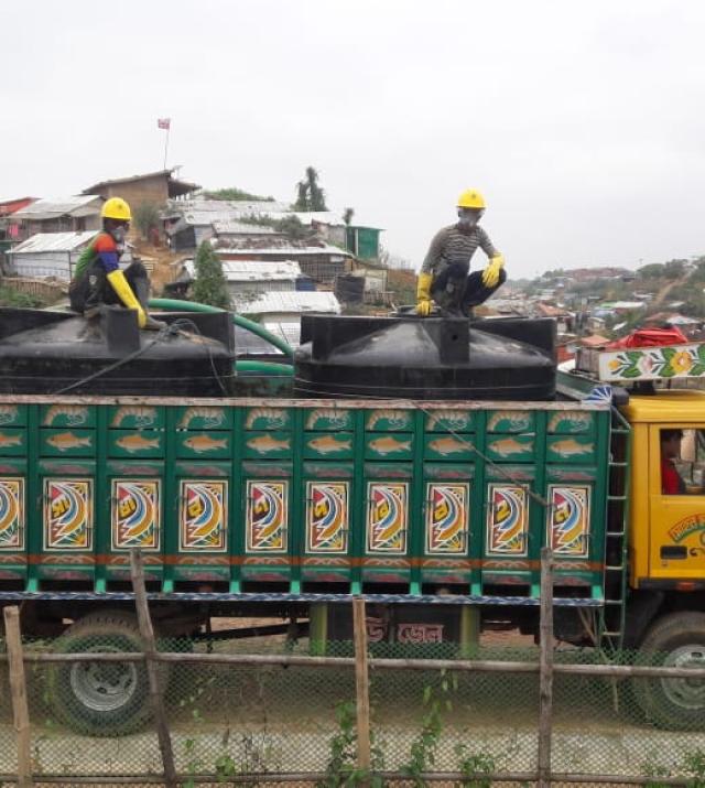A truck transports tanks with two man sitting above the tanks