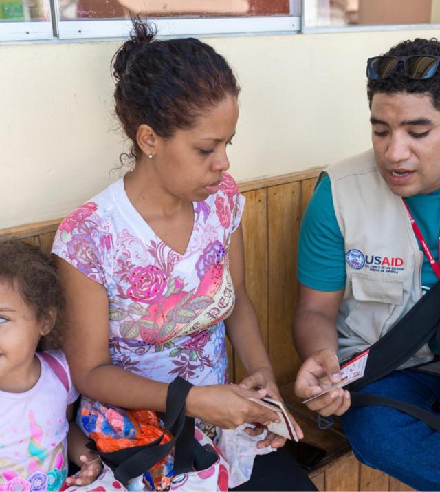 Project worker showing a woman who is sitting next to her child how to use a voucher.