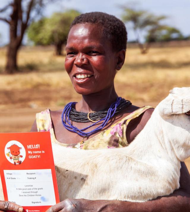 A woman is holding a white goat in her arms and an orange certificate in her hands.