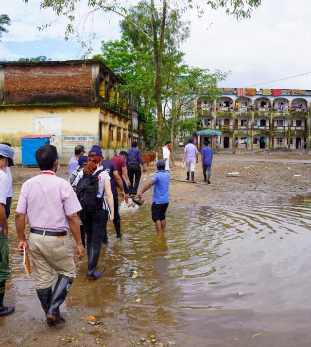A group of people walk through a flood waters toward a set of buildings