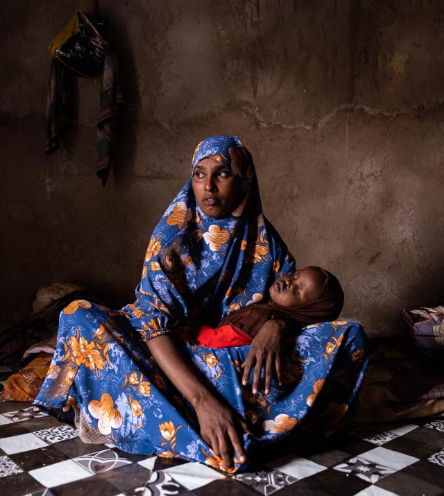 A woman sits on the floor with a child across her lap.