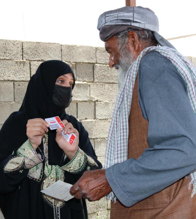 A man receives cash voucher food assistance from a woman wearing a black burqa