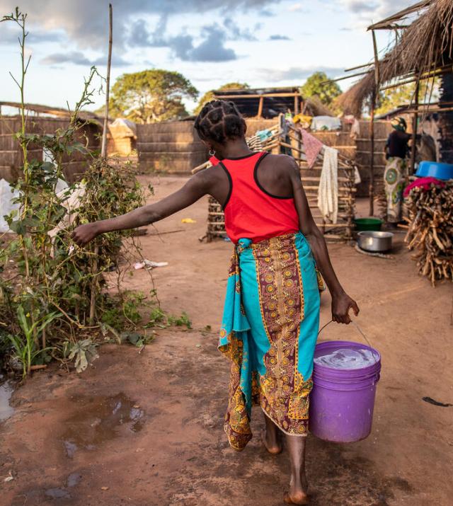 A woman carries a bucket of water with her back facing the camera.