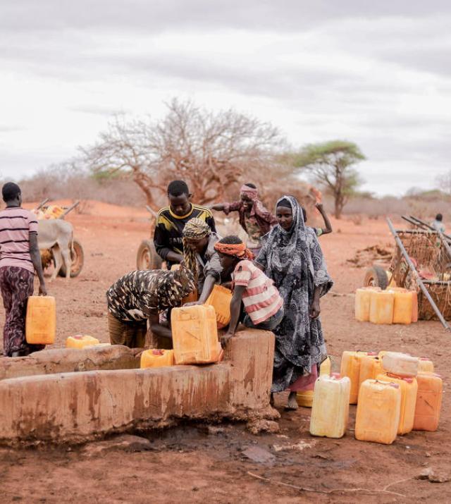 A group of people collect water from a trough using yellow bidons.