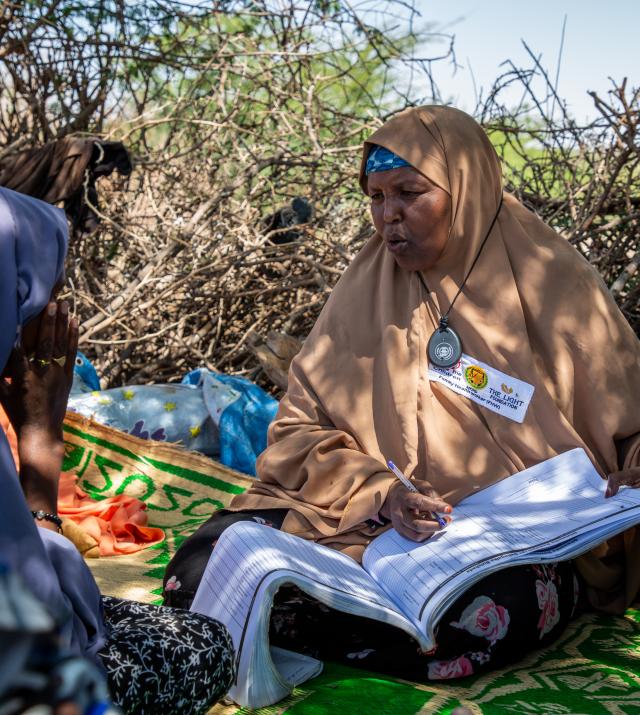 A woman wearing a tan headwrap records information in a paper booklet while conducting a MUAC test in Somaliland