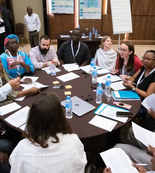 A group of people sit around a table during a stakeholder consultation. There are workshop materials at the table and the people are in active discussion.