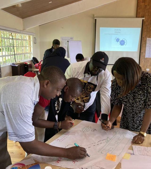 A group of people stand around a table writing on a large piece of paper during a workshop.