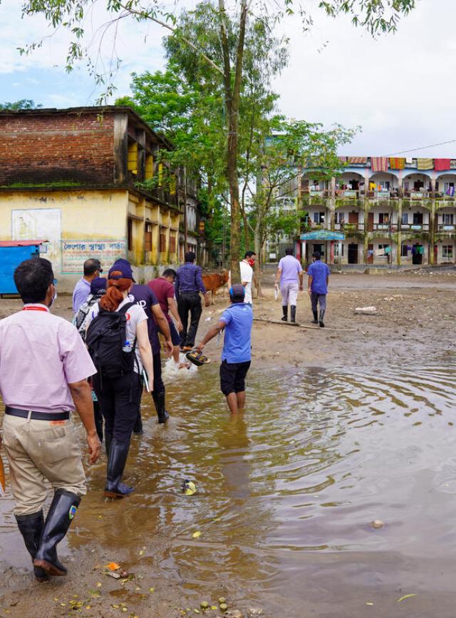 A group of people walk through a flood waters toward a set of buildings