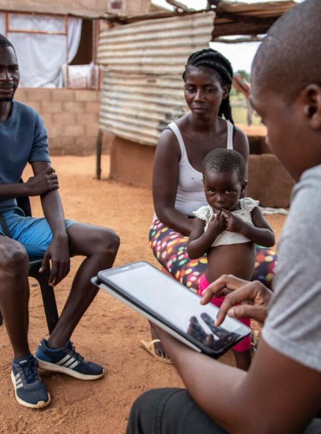 A man speaks with another man, woman, and child, and takes notes on an iPad.