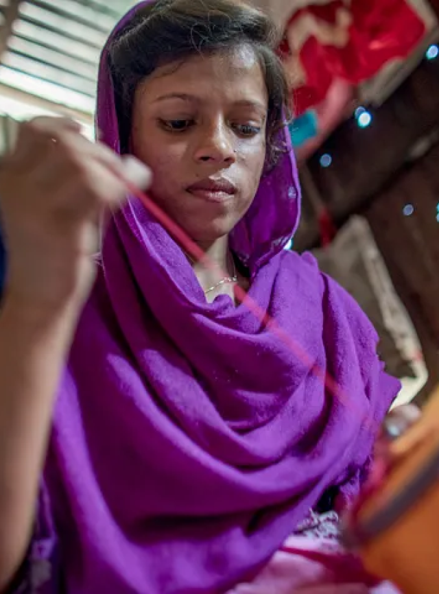 A young woman wearing purple pulls a needle and thread.