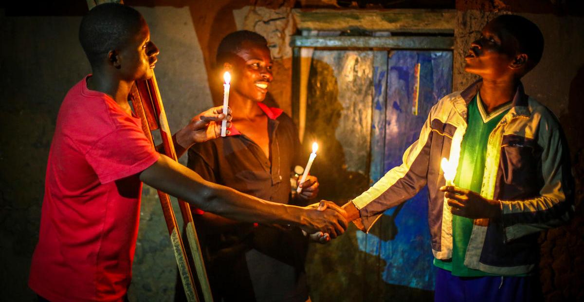 Three young men shake hands while holding a candle each.