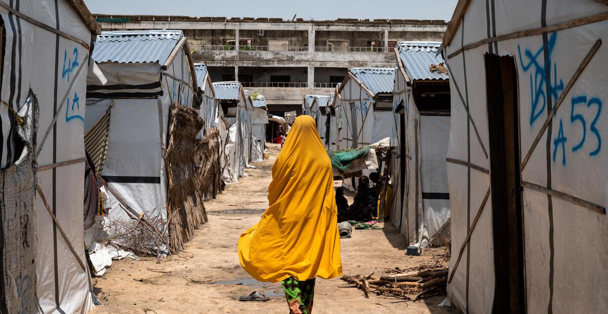 A young woman wearing yellow walks past tents in an IDP camp