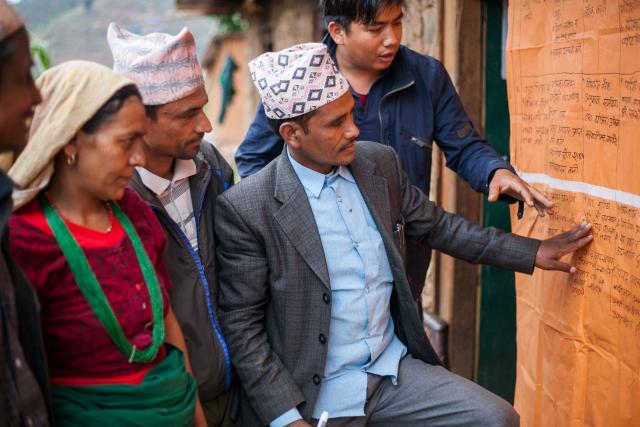 Photo of three Nepalese men and one woman looking and pointing to a posterboard