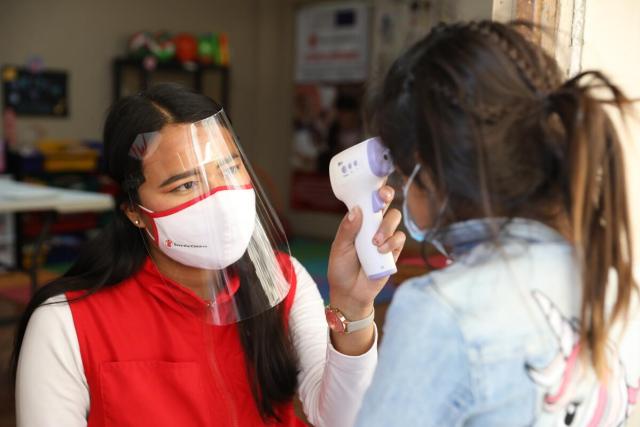A woman with a mask and face shield takes a child's temperature