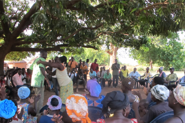 A group of about 30 people sit outside watching a demonstration.