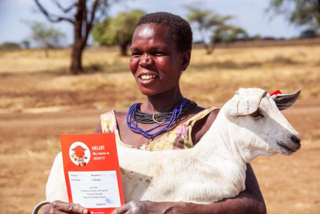 A woman is holding a white goat in her arms and an orange certificate in her hands.