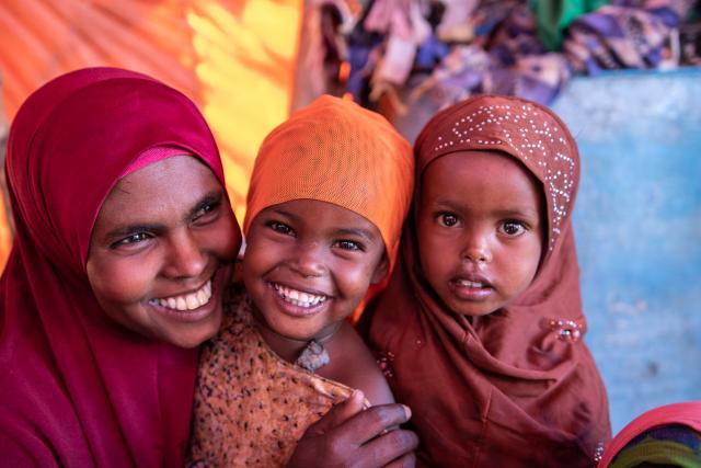 A woman in a hijab holding two young girls in hijabs smiling