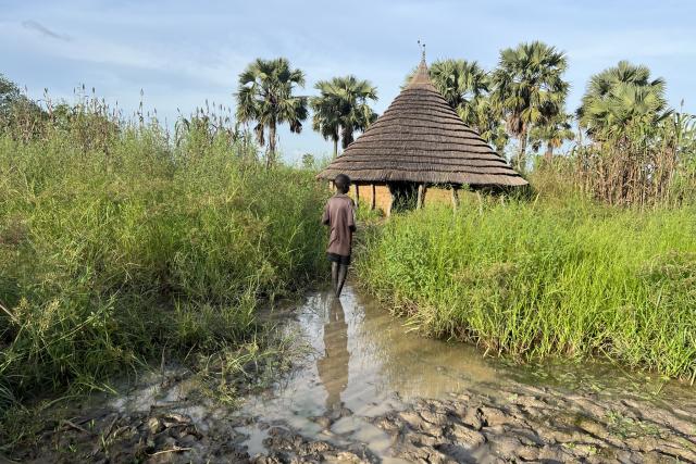 Young boy stands in front of a flooded house in South Sudan
