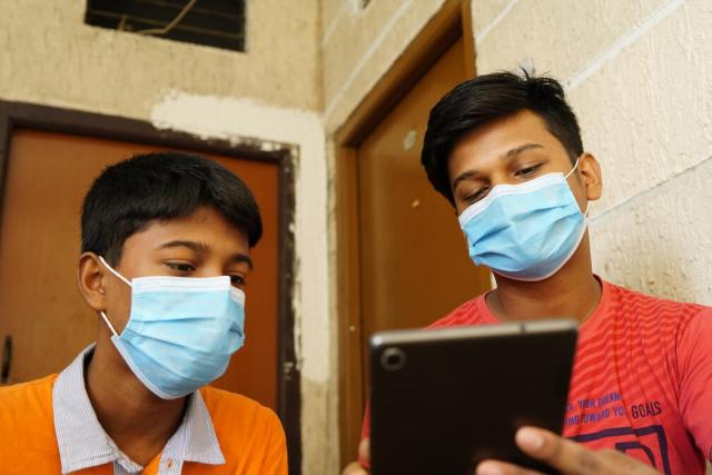 Two young men wearing face masks look at a tablet screen.