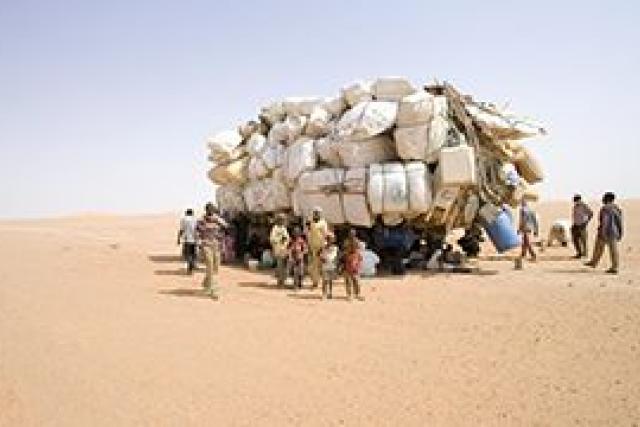 A truck loaded with white-wrapped items accompanied by people walking alongside it.