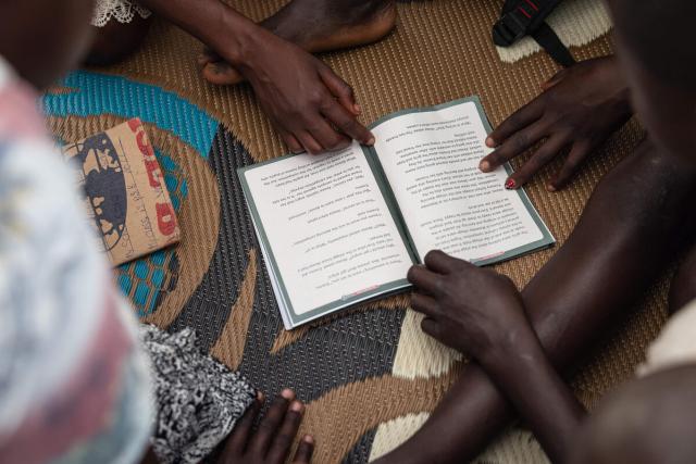 Children gather around a book, pointing with their fingers.