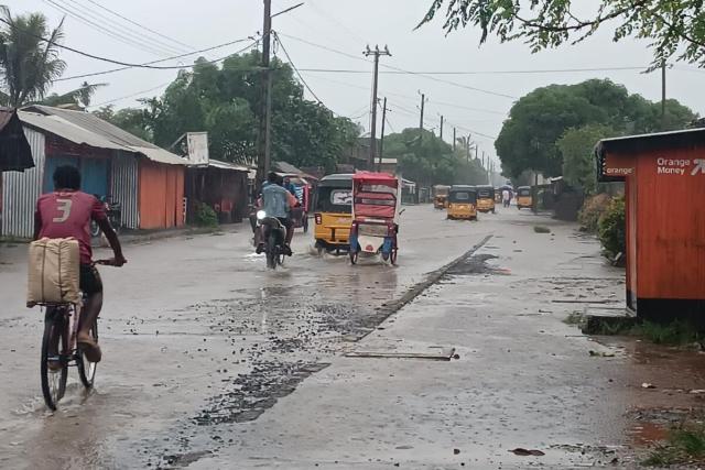 A bicycle, motorcycle, and threewheeler pass along a flooded road in Madagascar before a cyclone.