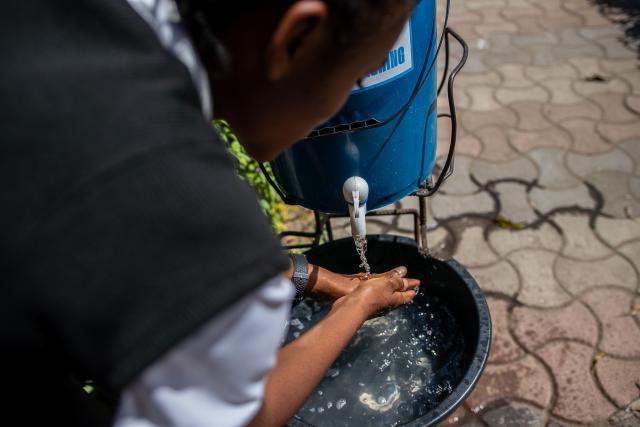 A girl leans over a bucket to wash her hands.