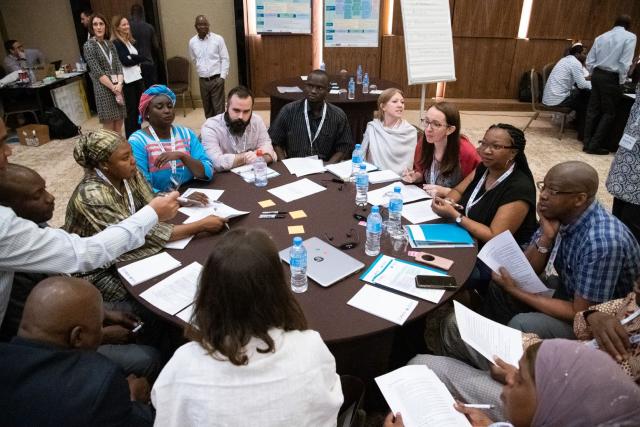 A group of people sit around a table during a stakeholder consultation. There are workshop materials at the table and the people are in active discussion.